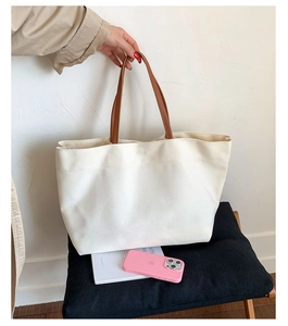 Minimalist cream canvas tote bag with brown leather handles next to an iPhone for scale