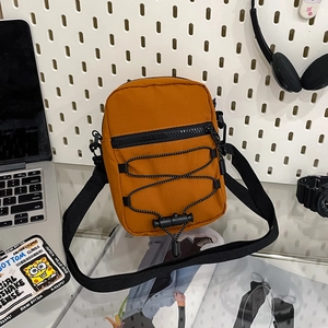 Detail of burnt orange nylon crossbody bag with black drawstring and adjustable strap