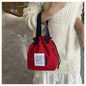 Detail of red canvas lunch bag with drawstring closure and navy blue webbing handle