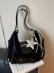 Sac hobo noir verni avec pendentif étoile argentée sur un support minimaliste blanc