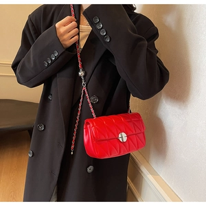 Detail of red quilted shoulder bag with silver chain strap on a black blazer
