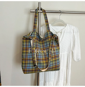 Detailed view of checkered canvas tote bag with FORYOUNG text on a white lace dress background