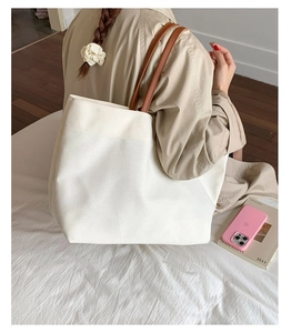 Detail of a minimalist canvas tote bag with brown leather straps in a lifestyle setting