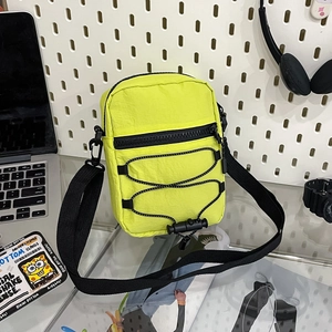 Macro detail of neon yellow nylon crossbody bag featuring black zippers and bungee cords