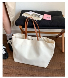 Detail of the magnetic snap closure on a large white canvas tote with leather handles