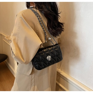 Detail of a black quilted leather crossbody bag with silver lock and metal chain strap