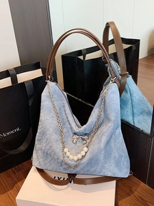 Blue denim shoulder bag with brown leather handles and pearl bow detail in a studio setting