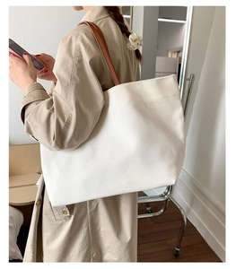Detail of white canvas tote bag with brown leather handles worn over a trench coat