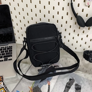 Detail view of black nylon crossbody bag with elastic drawstring on white pegboard