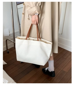Minimalist canvas tote bag with brown leather handles carried by a model in a lifestyle setting