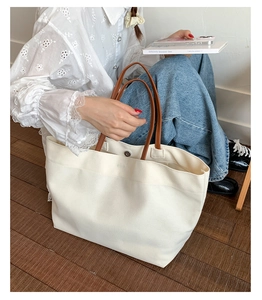 Detail of canvas tote bag showing cream fabric, brown leather handles and spacious interior