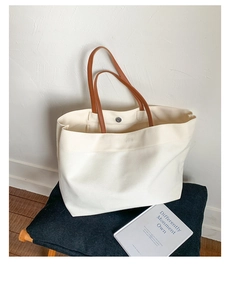 Detailed view of canvas tote bag with brown leather handles and silver snap fastener