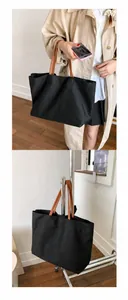 Detail view of a large black canvas tote bag with brown leather handles for daily use