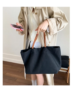 Minimalist black tote bag featuring long brown shoulder straps shown in a lifestyle setting