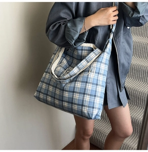 Detail of blue and white plaid canvas tote bag worn by model on a shoulder strap