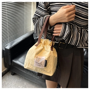 Detail of light yellow drawstring lunch bag featuring brown strap and stylish woven labels