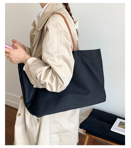 Black canvas tote bag with brown leather straps shown on a model in beige coat