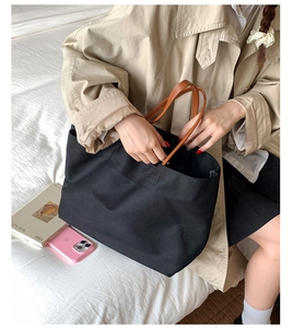 Detail of black canvas tote bag with brown leather handles on neutral background