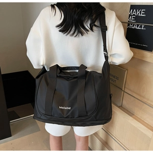Model wearing a large black expandable travel bag with shoulder strap and brand logo
