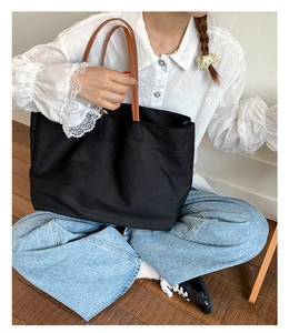 Fashionable black canvas tote bag with brown leather straps shown on a female model