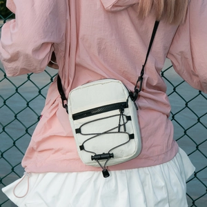 White nylon crossbody bag detail with black elastic cords shown on a model outdoors