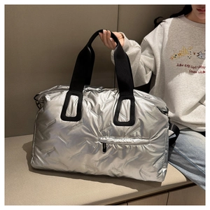 Detail of silver quilted travel bag featuring metallic finish and black woven handle straps