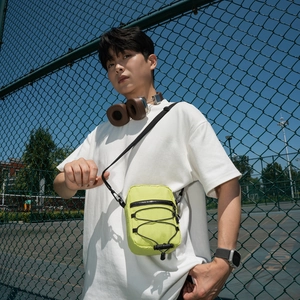 Close-up of neon green nylon crossbody bag with black bungee cords and adjustable strap