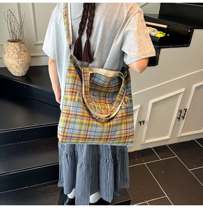 Model wearing yellow and blue plaid canvas tote bag with FOR YOUNG print in a warm indoor setting