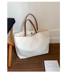 Detail of the white canvas tote bag showing brown leather handles and magnetic closure