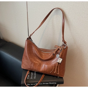 Detail view of retro brown PU leather shoulder bag with H.SHAY embossed logo and tassel