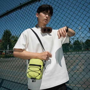 Detail of neon green nylon crossbody bag featuring black bungee cord and sports styling