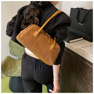 Brown suede baguette bag with leather trim held by a model in a stylish setting