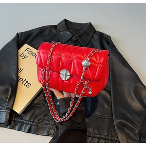 Detail of red quilted crossbody bag with silver ball chain and turn-lock closure