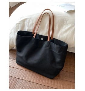 Detail of black canvas tote bag with brown leather handles and magnetic metal closure