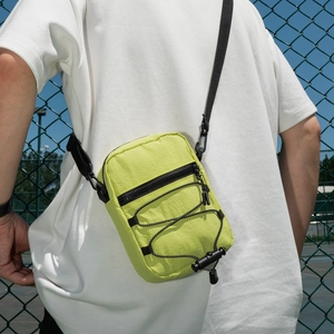 Detail of neon green nylon crossbody bag featuring black drawstring on green fence