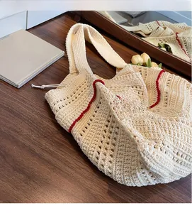 Close-up of cream knit tote bag with red contrast trim on dark wood surface