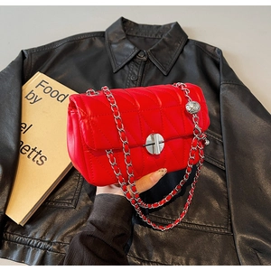 Close-up of red quilted crossbody bag with metal turn-lock and chain strap on leather