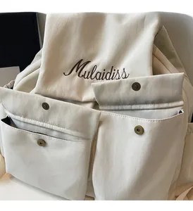 Detail of cream backpack with metal buckles and Mulaidiss embroidery on durable fabric
