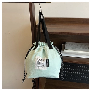 Detail of light green drawstring bucket lunch bag hanging on a minimalist wooden shelf
