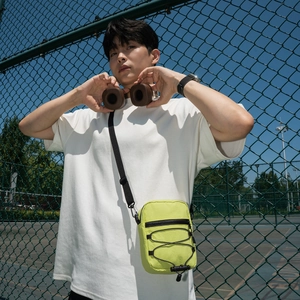 Neon green nylon crossbody bag with black drawstring detail on outdoor model
