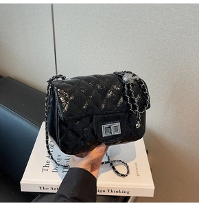 Détail d'un sac en cuir verni noir matelassé avec chaîne argentée et ornement boule