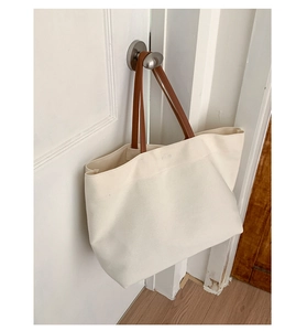 Detail of canvas tote bag showing beige fabric texture and brown leather handles