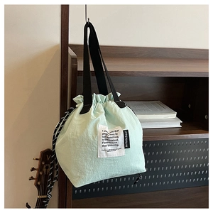 Detail of mint green drawstring tote bag with black handles and text label detail