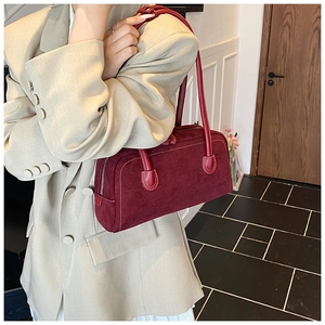 Detail of burgundy suede baguette bag with white stitching held by a model in a beige suit