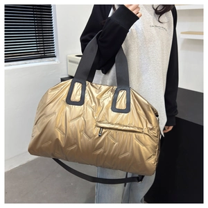 Detail of gold quilted travel bag with black handles and metallic puffy texture