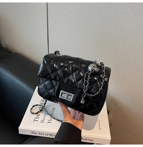 Détail d'un sac matelassé noir avec fermoir rotatif argenté et pendentif crâne décoratif