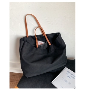 Close-up of black canvas tote bag showing brown leather handles and spacious interior
