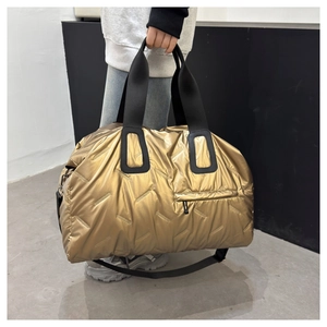 Detailed view of large gold quilted travel bag with black handles and shoulder strap