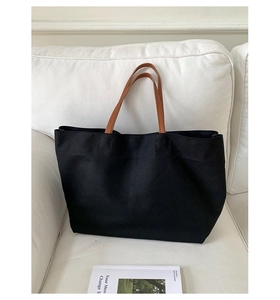 Detail of a minimalist black canvas tote bag with brown leather straps on a white sofa