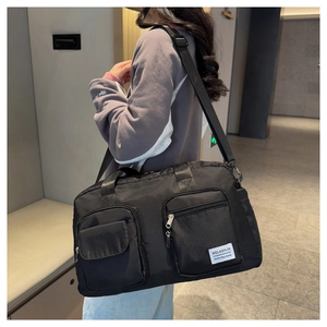 Detail view of the durable black nylon travel bag featuring front pockets and shoulder strap